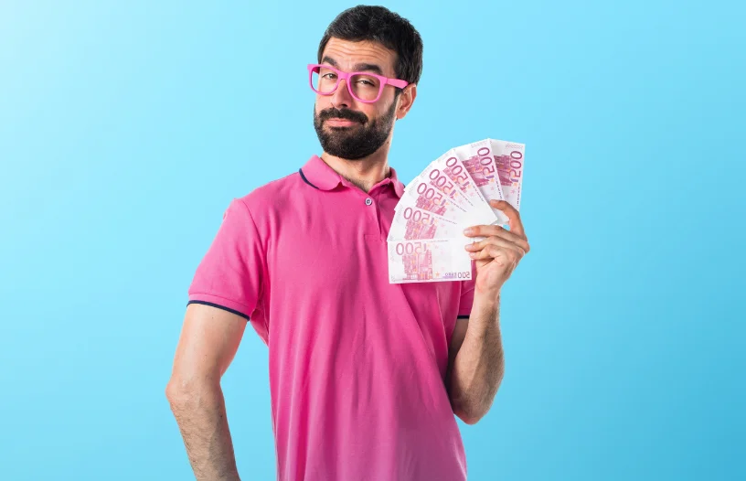 Homme avec un polo rose sur fond bleu qui tient des billets dans sa main gauche